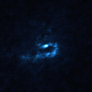 In this image a small ghostly figure lurks centrally in the frame on a dark background. The figure consists of blue blobs twisting downwards from the central bright region, forming a tight U-shape lying on its right side.