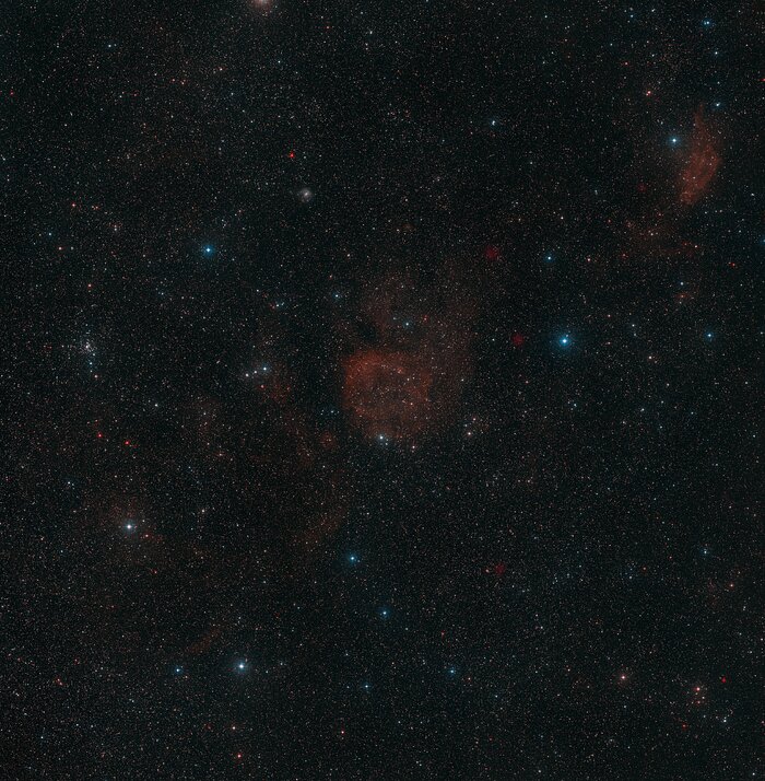 The image shows a dark area of night sky, speckled only lightly with the white and blue glow of stars. In the very centre is the orange cloud of the Sh2-284 nebula.