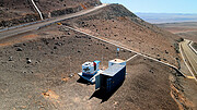 This image shows three shipping containers on a mountainside in a desert landscape. One of the containers is branded ‘DLR’, and is being worked on by a man on a ladder.