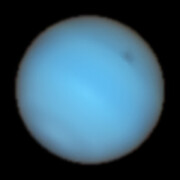 A telescopic image of the planet Neptune. It’s an almost-featureless cyan disc with a faint dark spot to the upper-right.