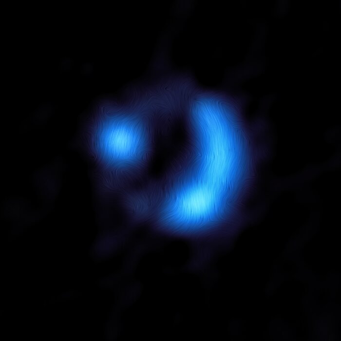 Located centrally on a dark background is an electric blue donut-shaped blob, showing the orientation of the magnetic field of the distant galaxy. The bright donut is not complete, and there are only two main features. The lines of the magnetic field give it an almost furry texture. The right-hand side of the donut forms a bright, curved banana-like shape. Instead, on the left-hand side, there is another bright region, circular in shape.