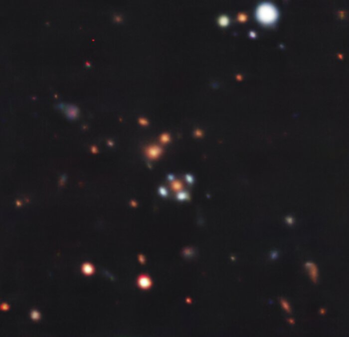 The cross pattern stands out over a dark background. Like a blue daisy with only four petals, the galaxy at the center is yellow, and around it are the four blue images of the background galaxy. Around the system are other galaxies, which appear as red or white dots.